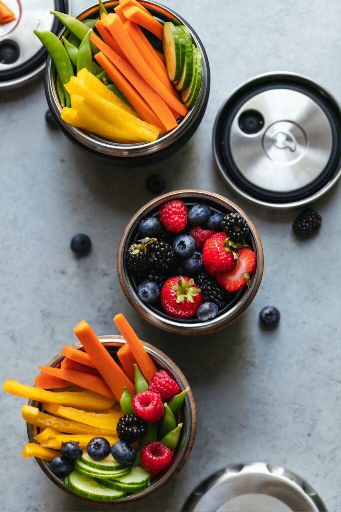 Three round containers of food filed with berries and vegetable sticks