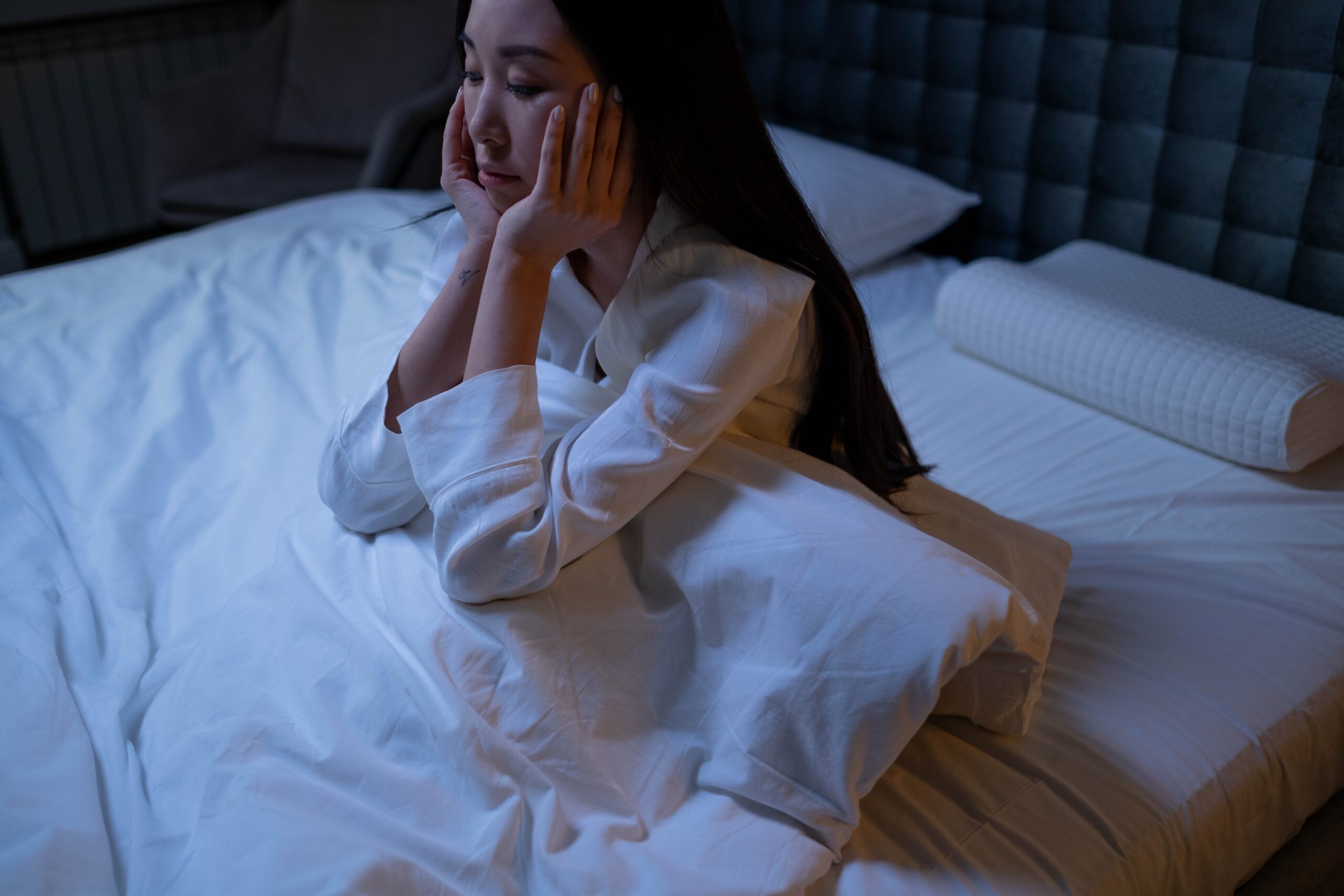 Woman wearing white long-sleeve shirt sitting on a bed at night